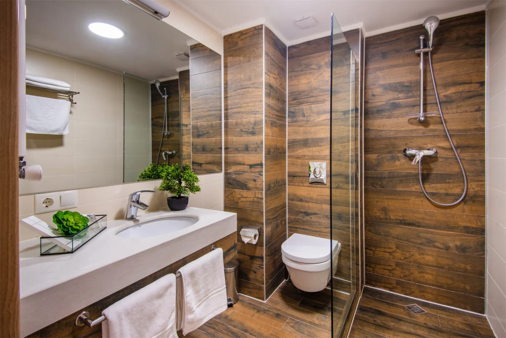 Orbi Palace Bakuriani — Modern bathroom with wood-look tile, glass shower and white vanity sink.