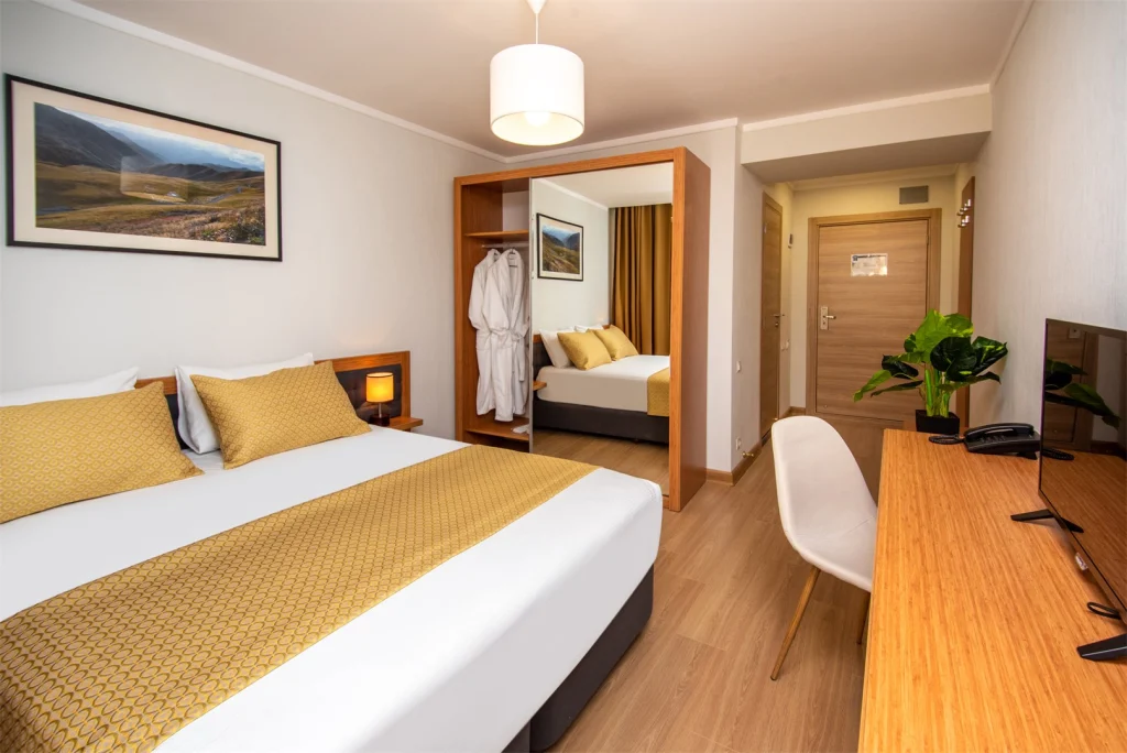 Orbi Palace Bakuriani — Hotel room with double bed, wardrobe mirror, desk and mountain artwork.