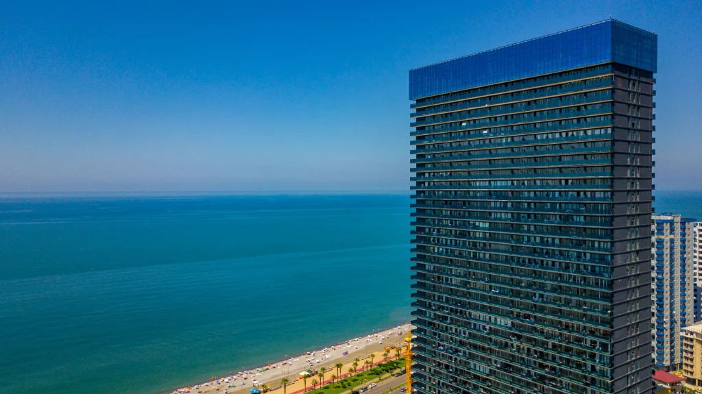 Orbi Residence Hotel — Tall glass tower overlooking the sea with coastline and beach visible below.