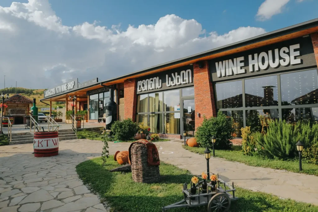 Patardzeuli Wine House — Front entrance of the Wine House with brick facade, patio seating, and decorative wine cart.