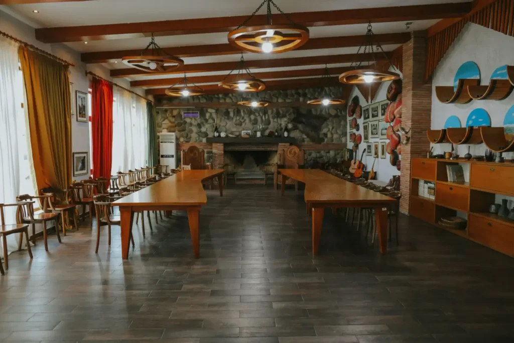 Patardzeuli Wine House — Dining hall with long wooden tables, beamed ceiling, and stone fireplace.