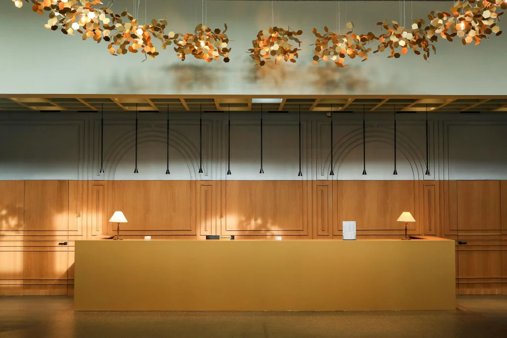 Pine Astoria — Hotel lobby with a wooden reception desk and decorative hanging ceiling fixtures.