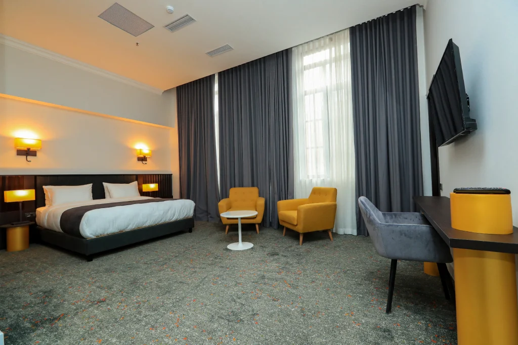 Pine Astoria — Spacious guest room with a king bed, yellow armchairs, and a wall-mounted TV.