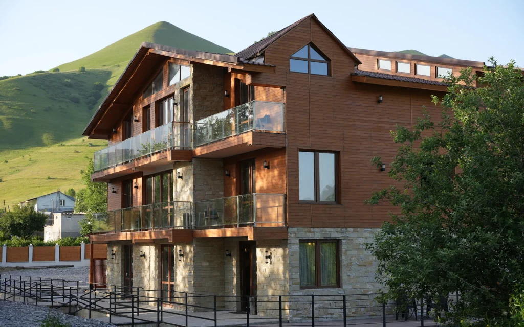 Pine Chalets By KA Group — Wooden chalet-style hotel building with balconies set against green hills.