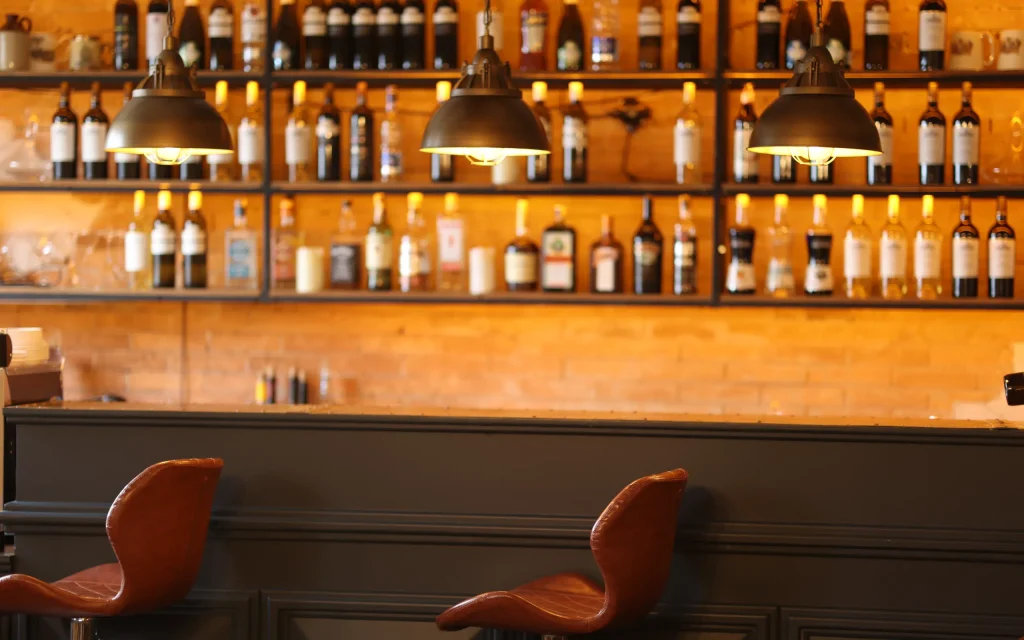 Pine Chalets By KA Group — Hotel bar area with stocked shelves, pendant lights and leather stools.