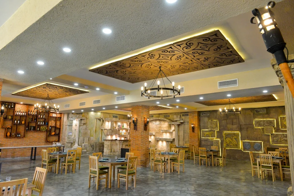 Prometheus Kvevri Wine Museum — Spacious restaurant with wooden tables, decorative stone walls, and ambient lighting.