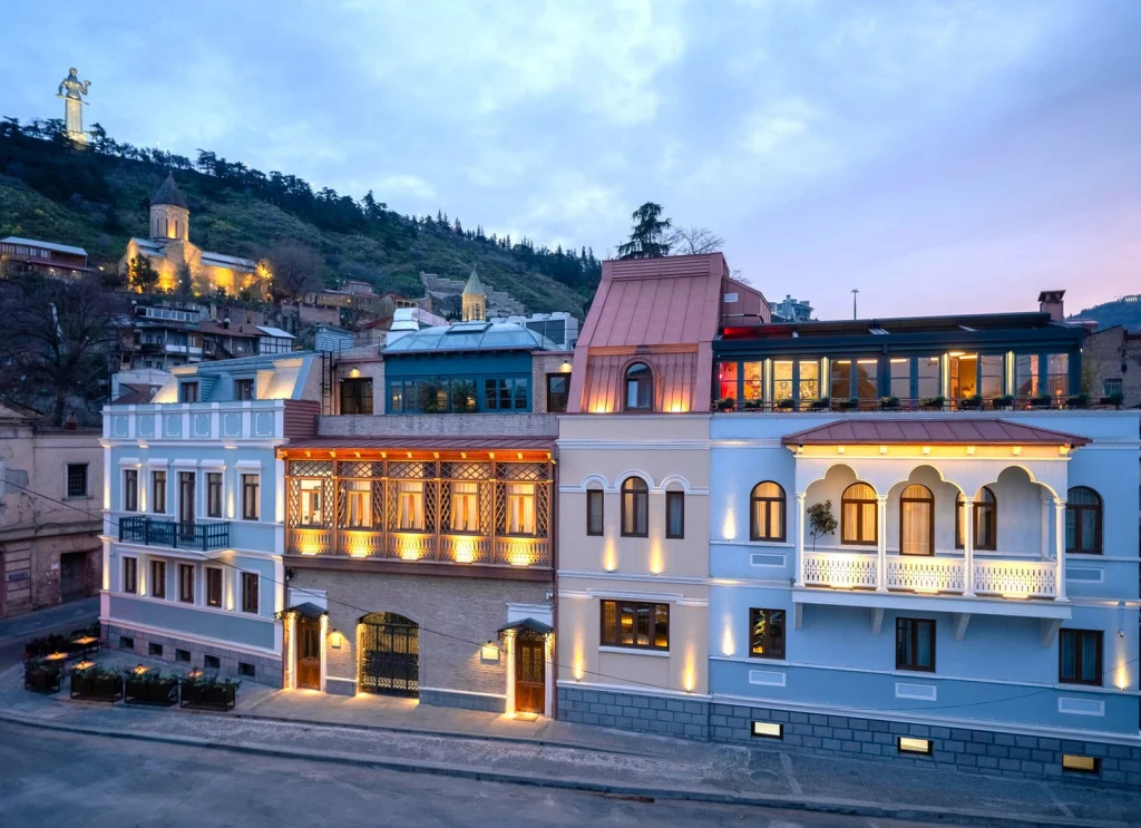 Puris Moedani Boutique Hotel — Illuminated hotel facade at dusk with balconies, set against a hillside townscape.