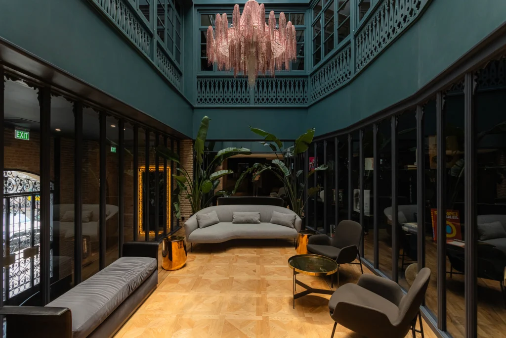 Puris Moedani Boutique Hotel — Elegant lobby lounge with glass walls, lush plants, and an ornate chandelier.