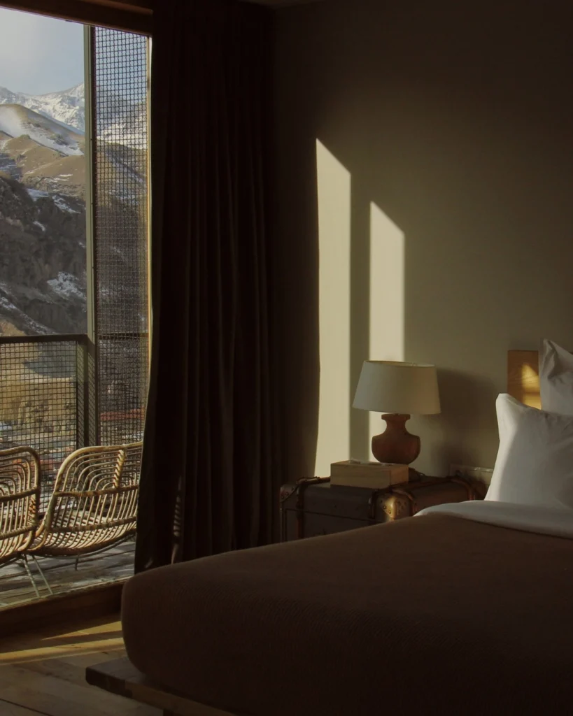 ROOMS Kazbegi — Hotel room with bed and large window overlooking snowy mountains.