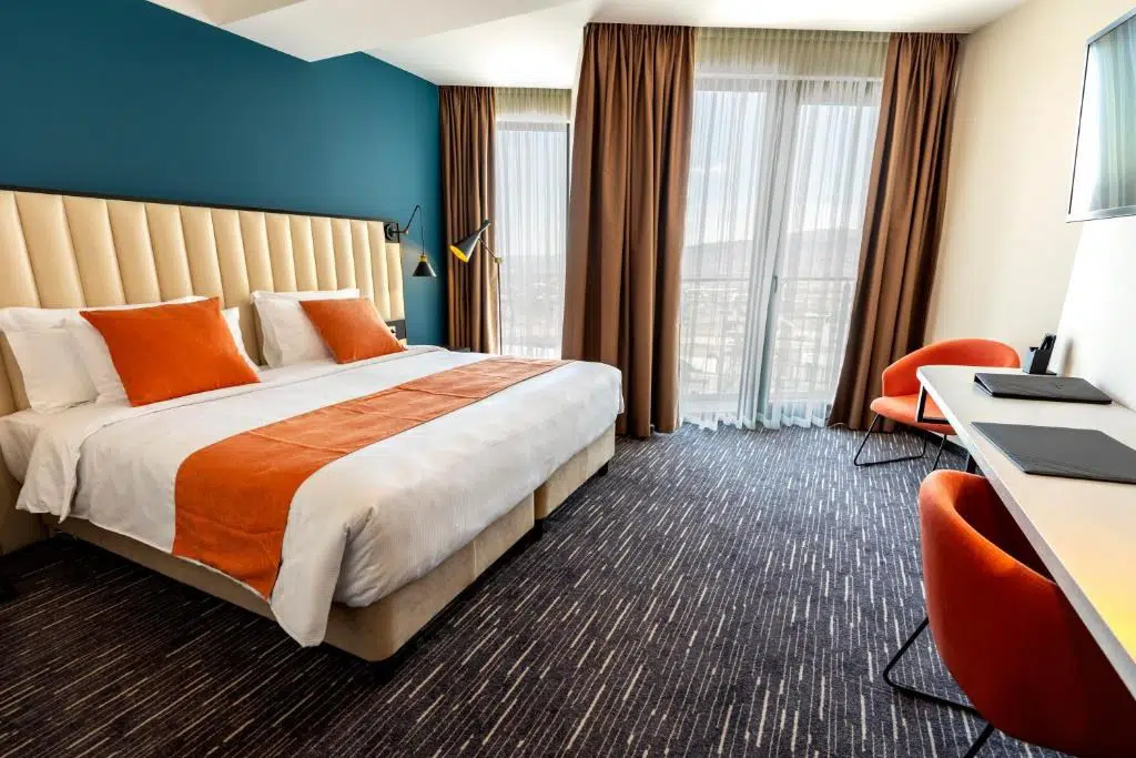 Sevsamora Resort & Spa — Hotel bedroom with orange-accented bedding, teal wall, and city-view balcony.
