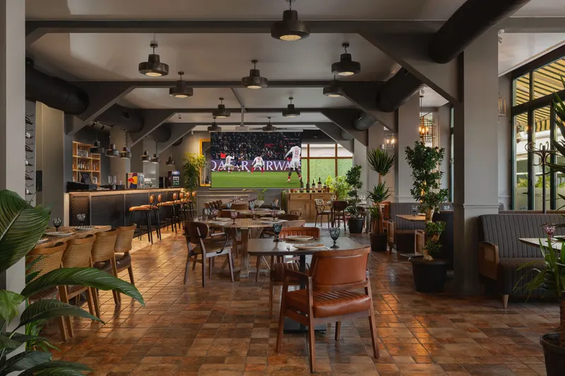 Shua Kalaki Arena — Indoor restaurant and bar area with wooden tables, leather chairs, and plants.