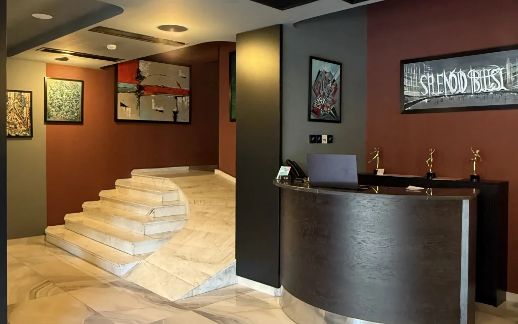 Splendid Tbilisi — Hotel reception desk with marble staircase and framed artwork in the lobby.