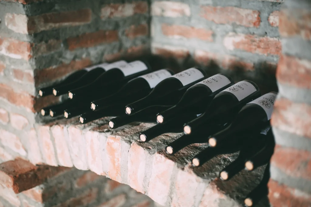 Teleda Orgo — Wine bottles resting on a brick shelf inside a stone cellar.