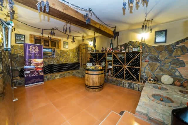 Tevza Winery — Stone-walled tasting room interior with wine racks, barrel table, and hanging decorations.
