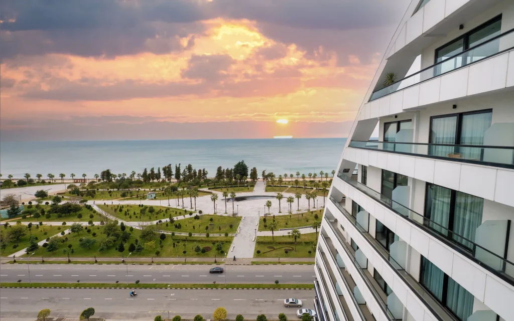 The Grandeur Hotel — Aerial view of the hotel building overlooking a seaside park and coastline at sunset.