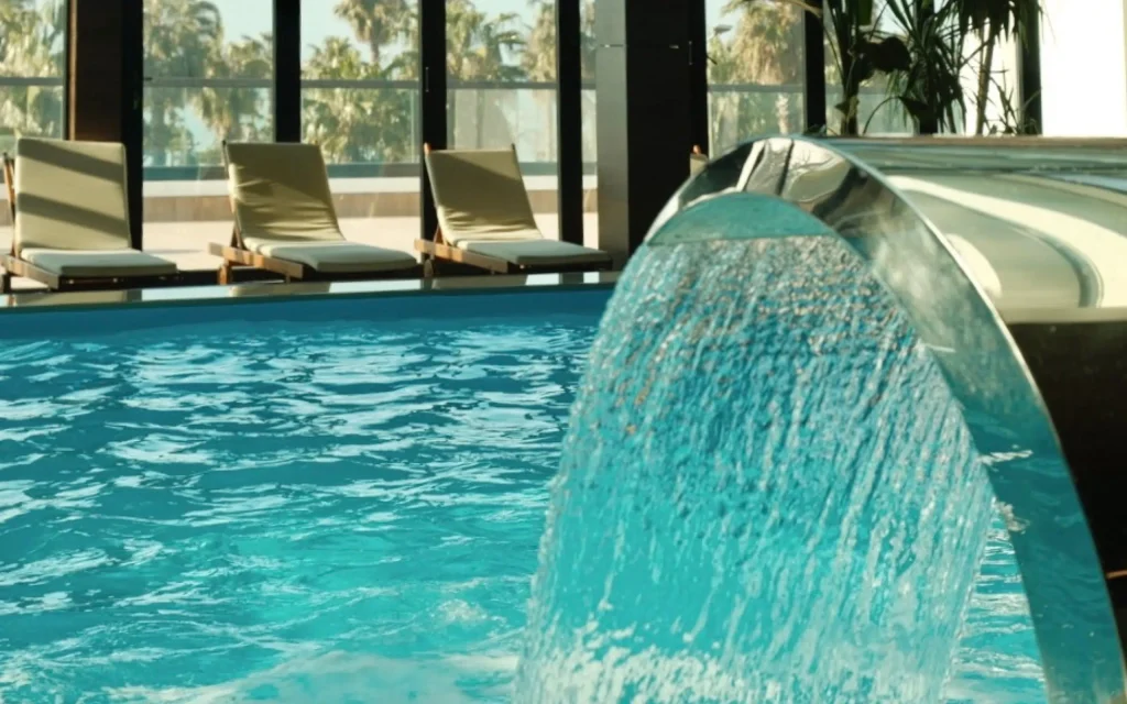The Grandeur Hotel — Indoor pool area with lounge chairs and a decorative water feature cascading into the pool.