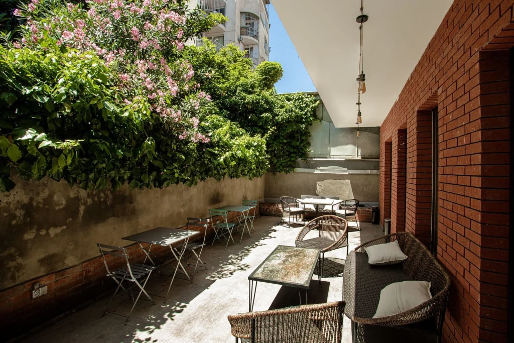 The Tbilisi Pod — Outdoor courtyard seating area with tables, chairs, brick wall, and greenery.