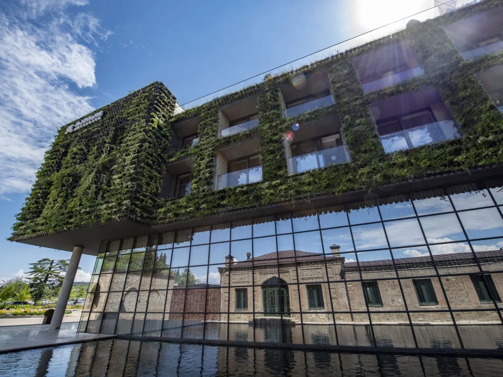 Tsinandali Estate, A Radisson Collection Hotel — Green-wall hotel facade with reflecting pool and historic stone building behind glass atrium.