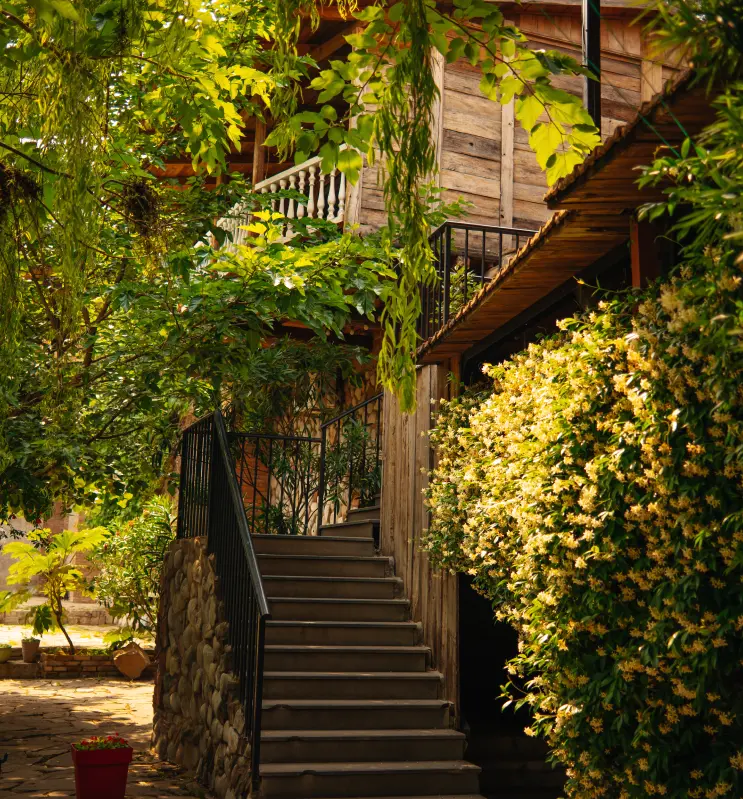 Tsiskvili in Mtskheta — Wooden exterior facade with staircase and balcony surrounded by lush greenery and flowers.