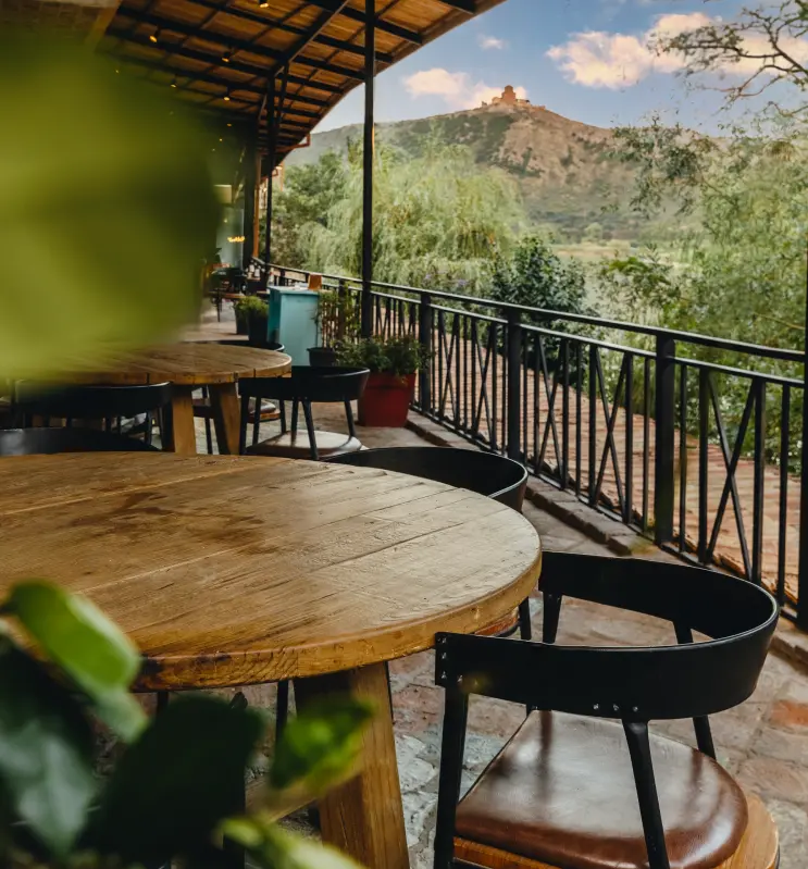 Tsiskvili in Mtskheta — Terrace dining tables overlooking a river valley with a hilltop monastery in the distance.