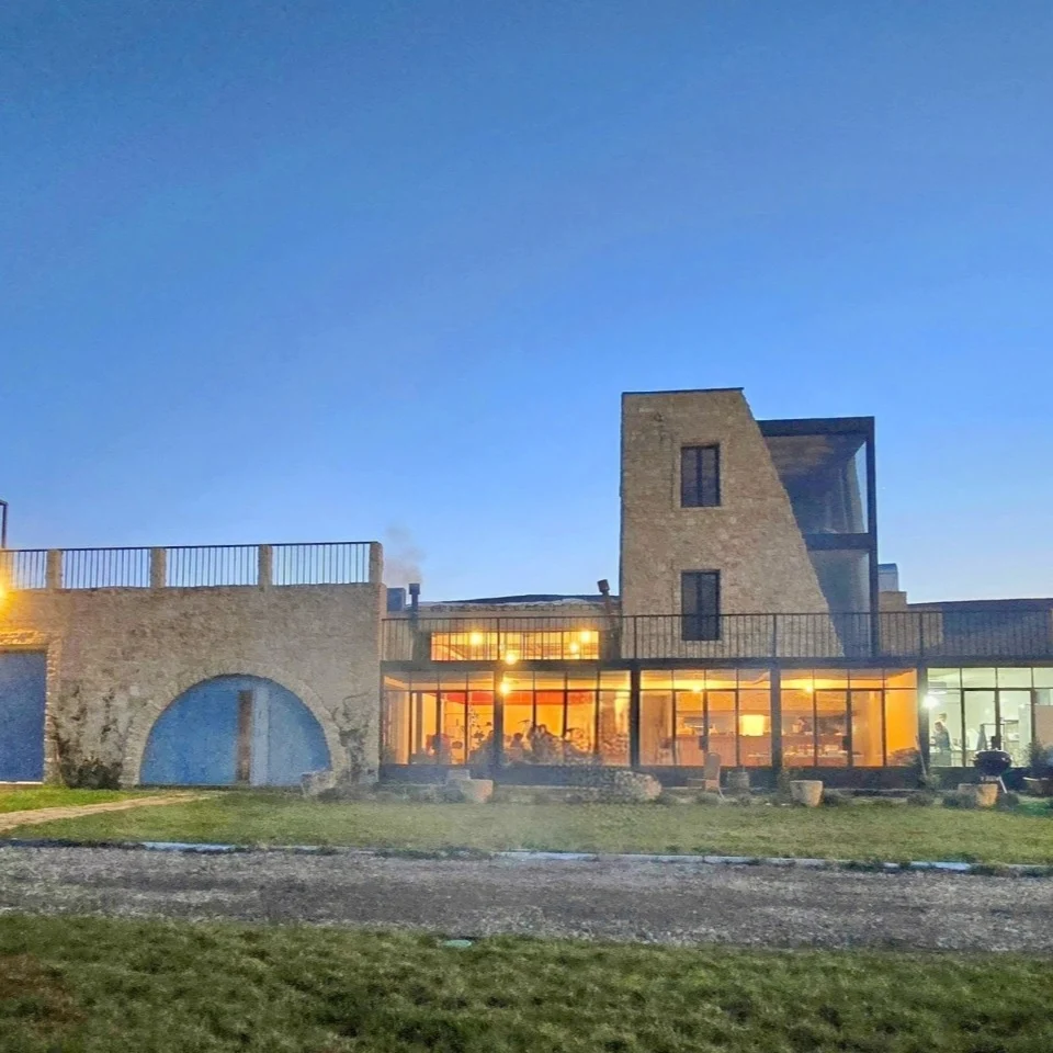 Uplistsikhe Estate — Illuminated estate building with glass facade glowing at dusk beside stone wall.
