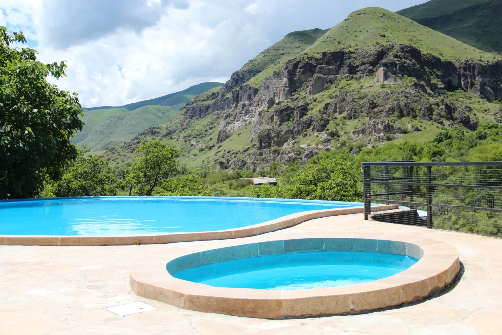 Vardzia Resort — Outdoor infirity-style pool and jacuzzi overlooking green mountains and cliffs.