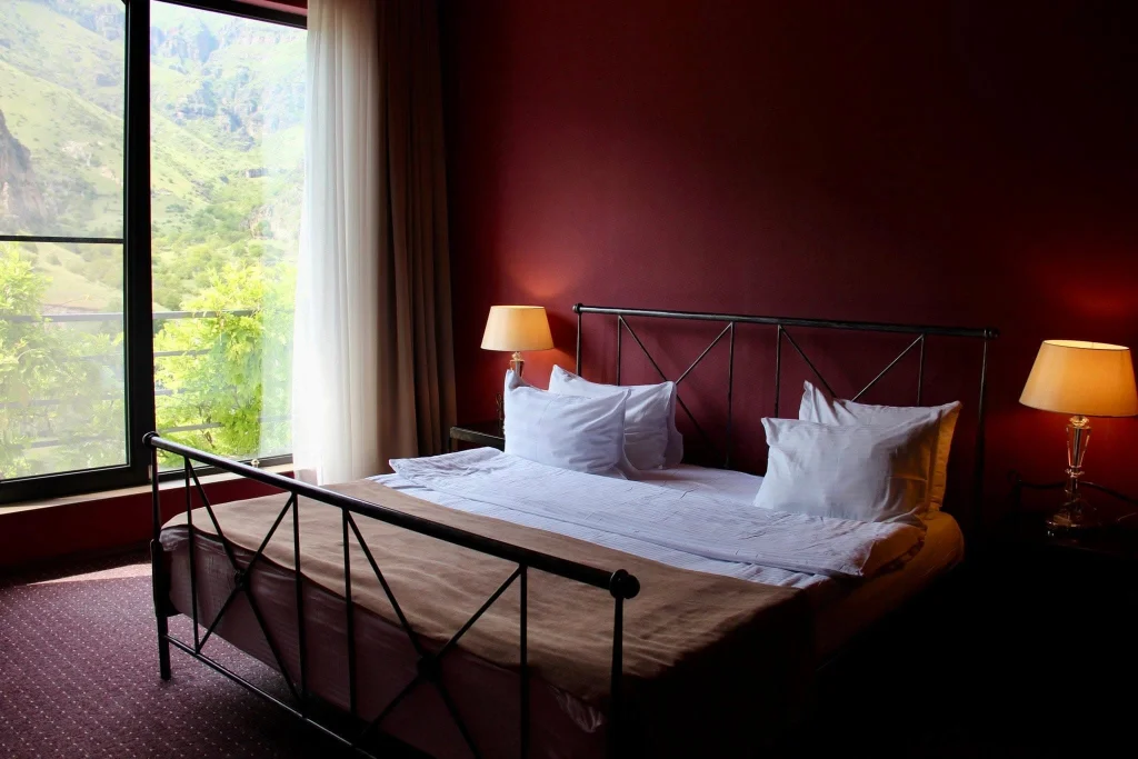 Vardzia Resort — Hotel room with iron-frame bed, red walls, and a mountain-view window.