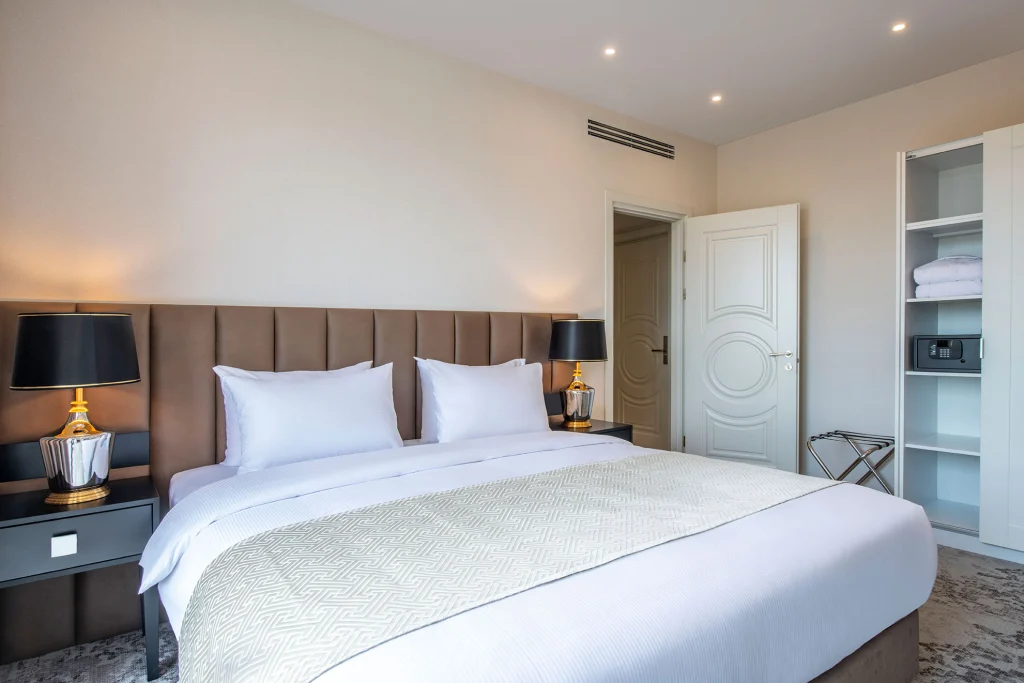 Villa Mosavali — Modern hotel bedroom with king bed, bedside lamps, and built-in wardrobe shelving.