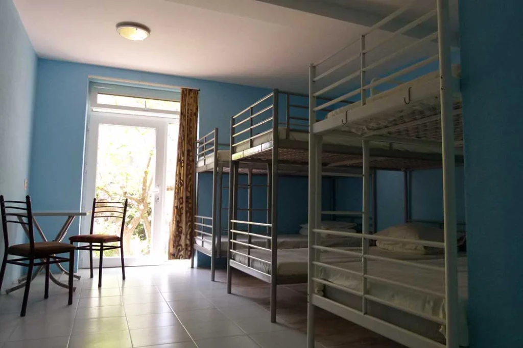 Why Me Tbilisi — Dormitory room with multiple metal bunk beds and a small seating table.