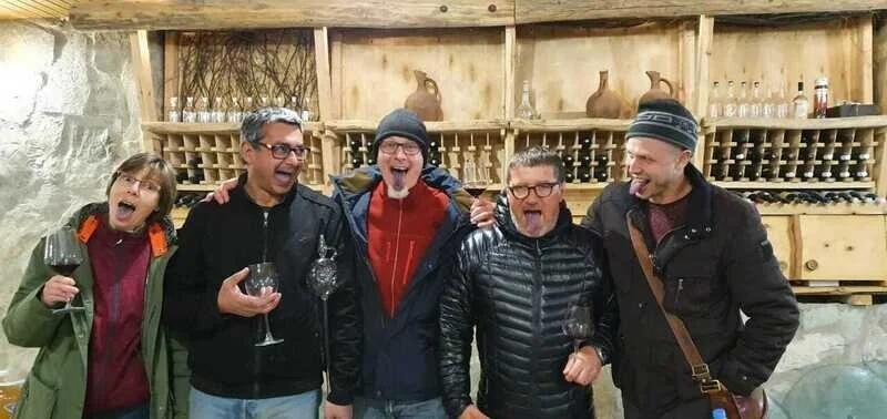 Wine Artisans — Visitors pose smiling in a stone wine cellar lined with bottles and barrels.