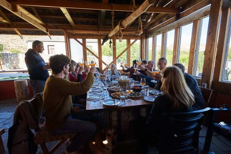 Wine Artisans — Guests raise a toast at a long communal table in a wooden dining pavilion.