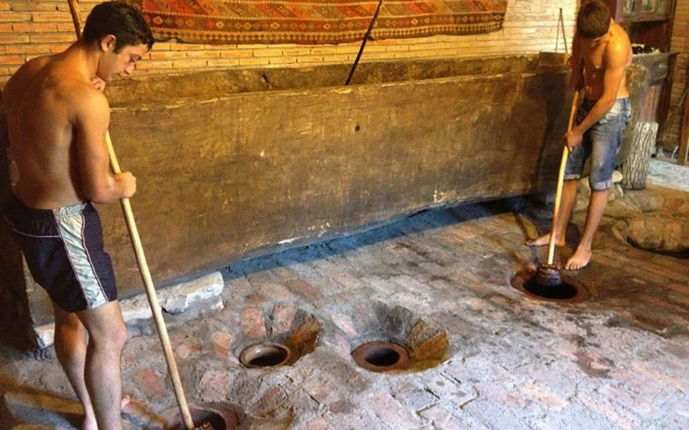 Wine House Gurjaani — Workers tread grapes in traditional clay pits inside the winery cellar.