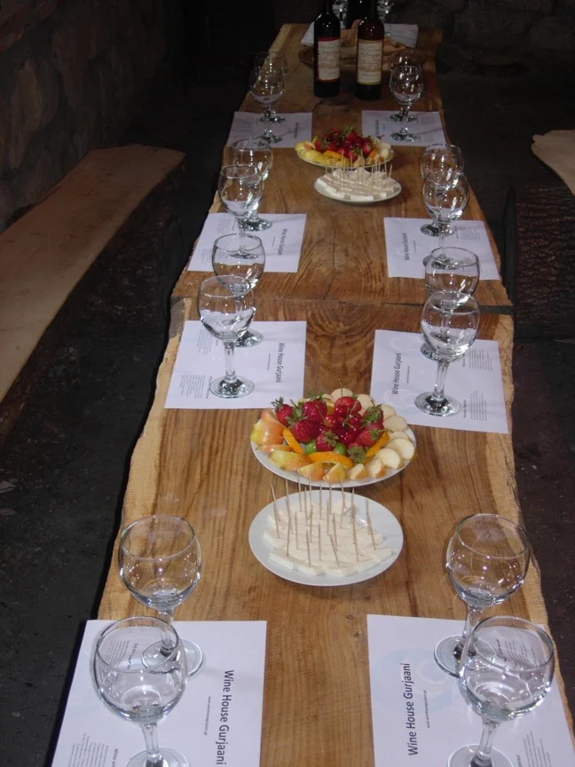 Wine House Gurjaani — A long wooden table set with wine glasses and fruit platters for a tasting.