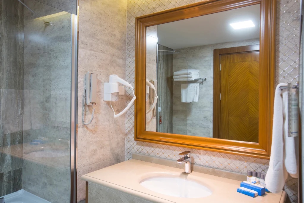 Wyndham Batumi — Bathroom with marble-tiled walls, glass shower enclosure, and vanity sink with mirror.
