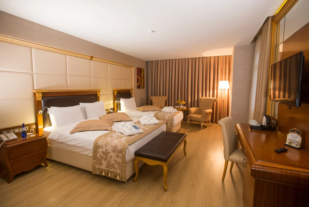Wyndham Batumi — Hotel room with twin beds, upholstered headboard, armchairs, and wood flooring.