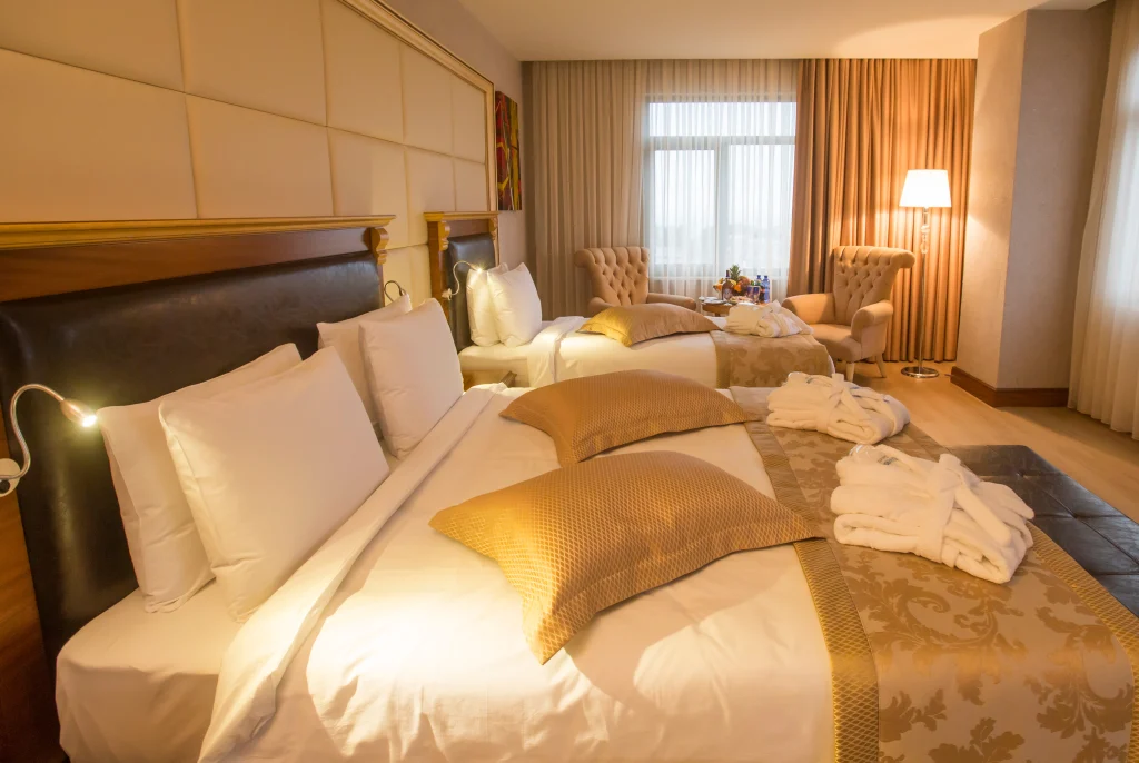 Wyndham Batumi — Spacious guest room with twin beds, gold-toned linens, and folded robes placed on the bed.