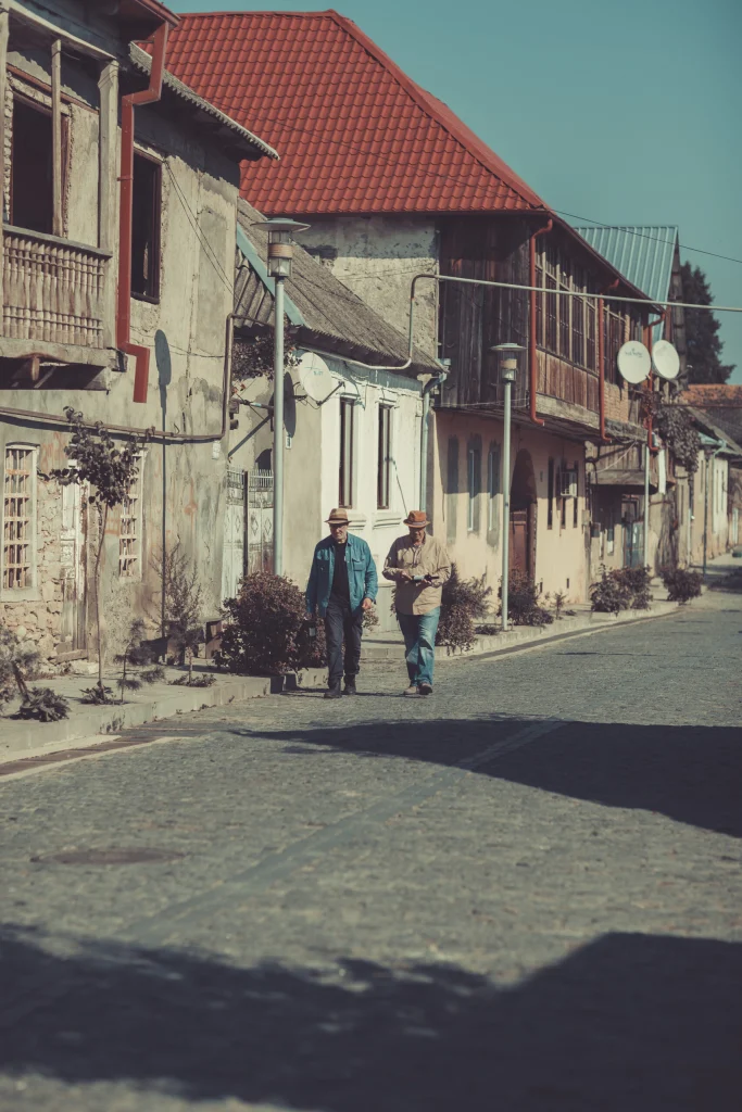 brothers cellar — Two men walk along a cobblestone street past old village houses.