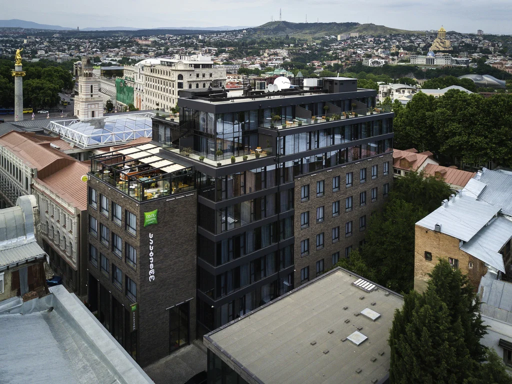 ibis Styles Old Tbilisi — Aerial view of the hotel building overlooking Tbilisi's cityscape and surrounding hills.