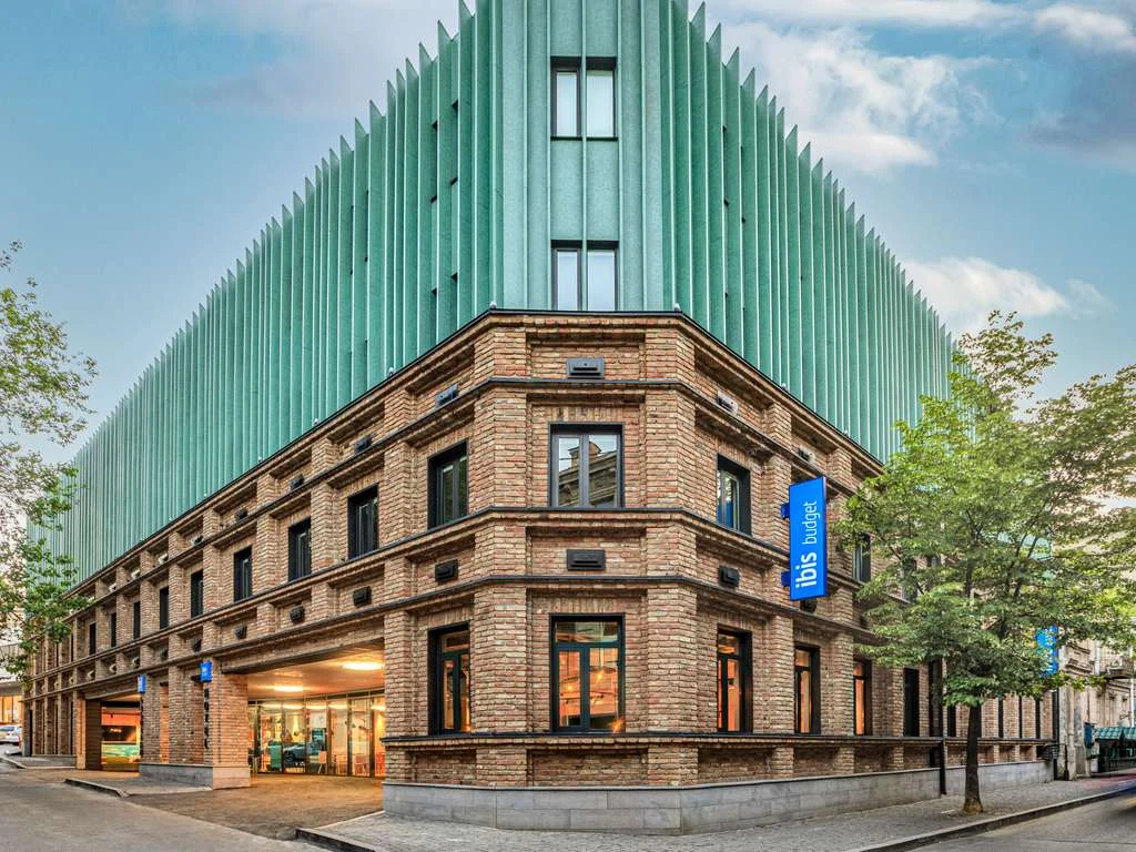ibis budget Tbilisi Center — Modern hotel exterior with brick facade and green vertical fin cladding on upper floors.