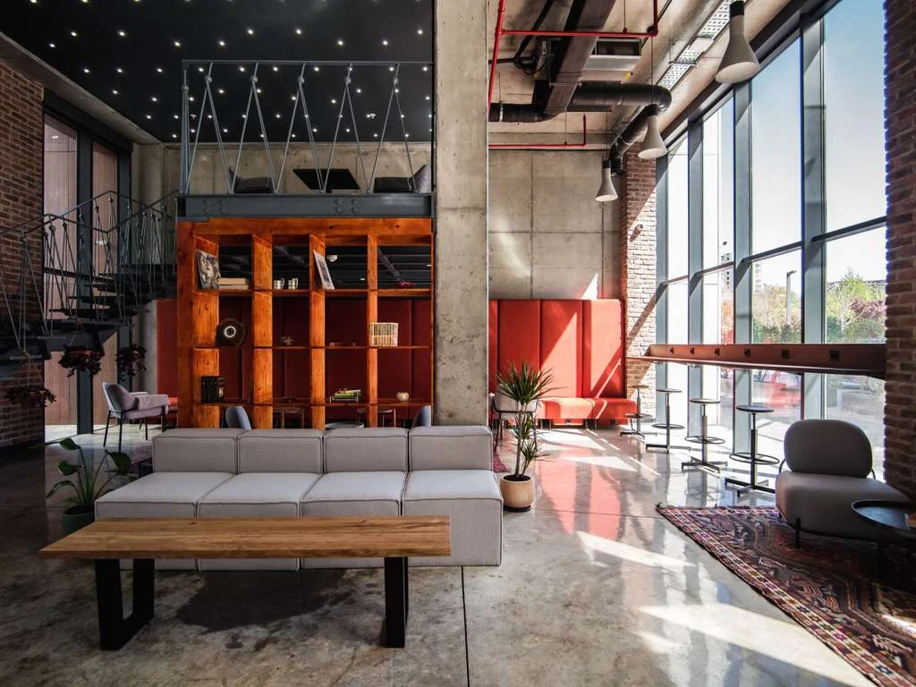 ibis budget Tbilisi Center — Industrial-style lobby lounge with concrete pillars, exposed pipes, and large windows.
