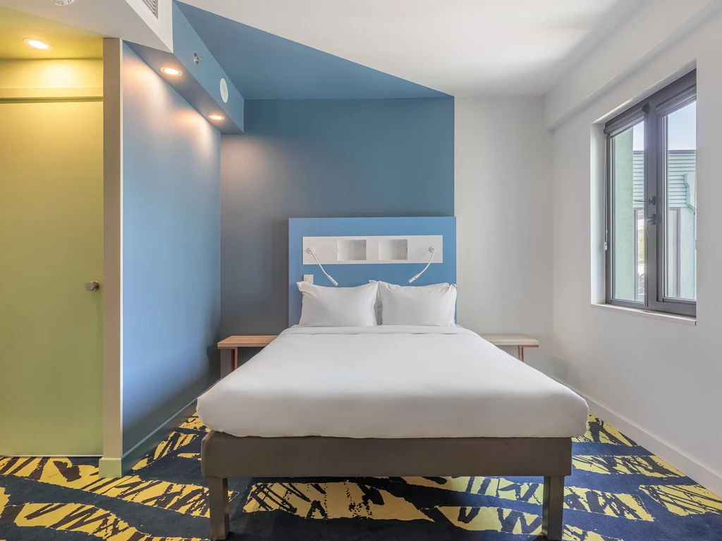 ibis budget Tbilisi Center — Bright guest room with double bed, blue accent wall, and large window.