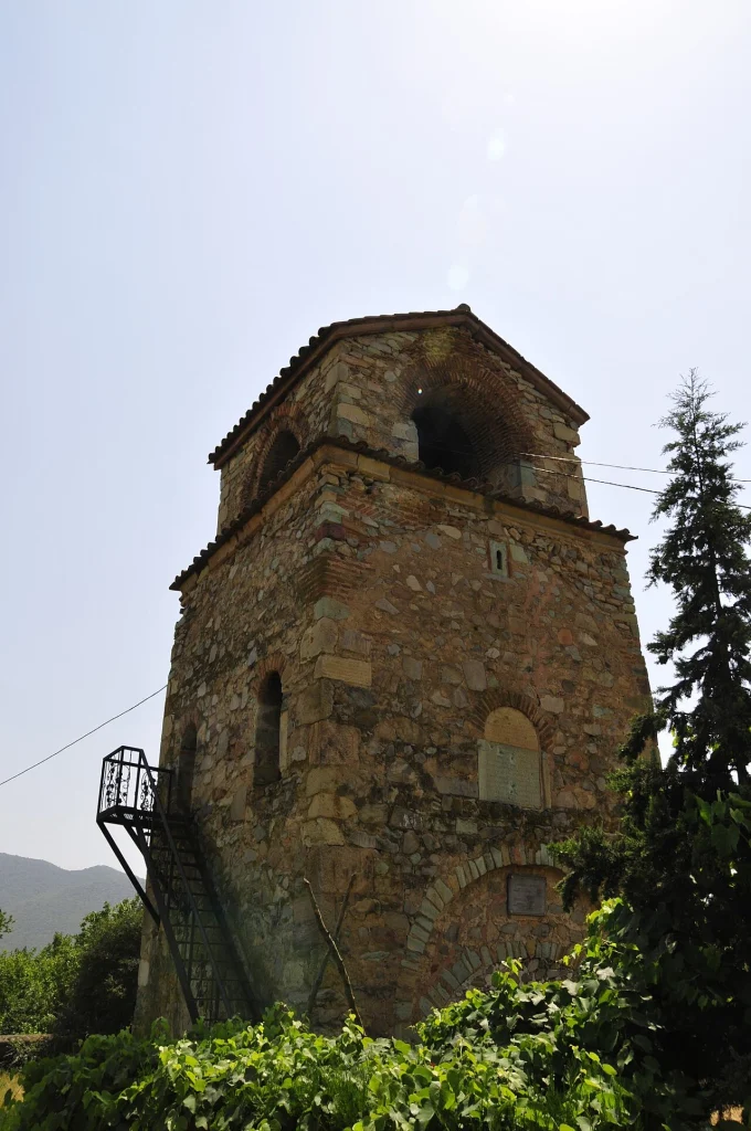An old stone bell tower church in Georgia surrounded by greenery and vineyards.