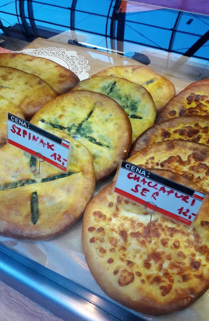 Freshly baked Georgian khachapuri with spinach and cheese fillings displayed on a bakery counter.
