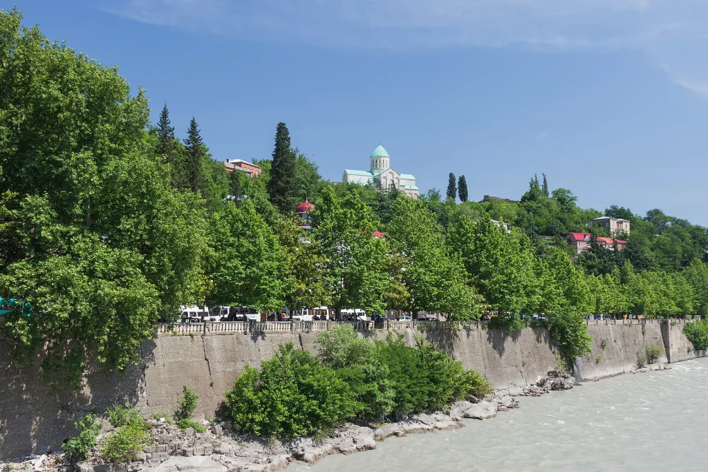 View of the Rioni River banks lined with trees and Bagrati Cathedral in the distance.
