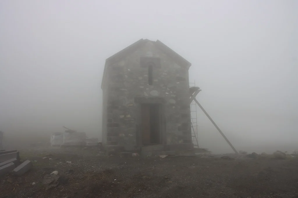 A stone chapel stands shrouded in mist near the summit of Abano Pass.