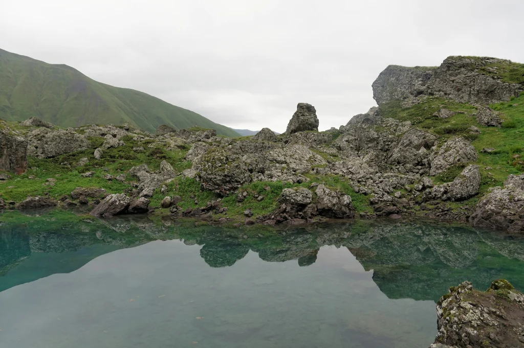 Turquoise Abudelauri Lake reflecting the rocky slopes at the foot of the Chaukhi Massif.