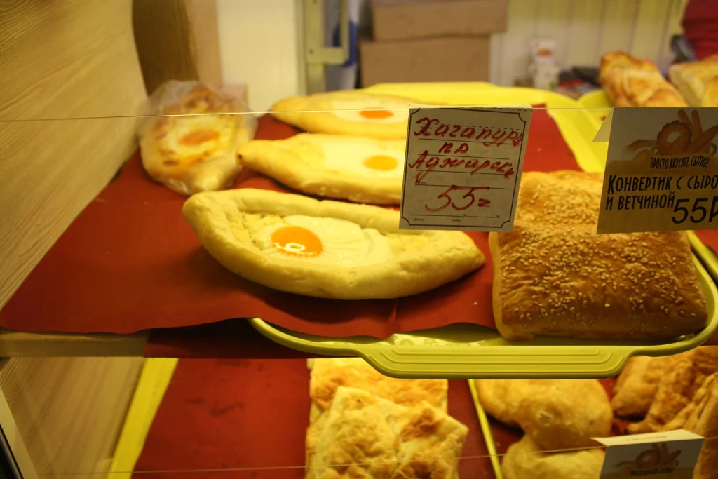 Adjarian khachapuri pastries with egg filling displayed in a bakery case.