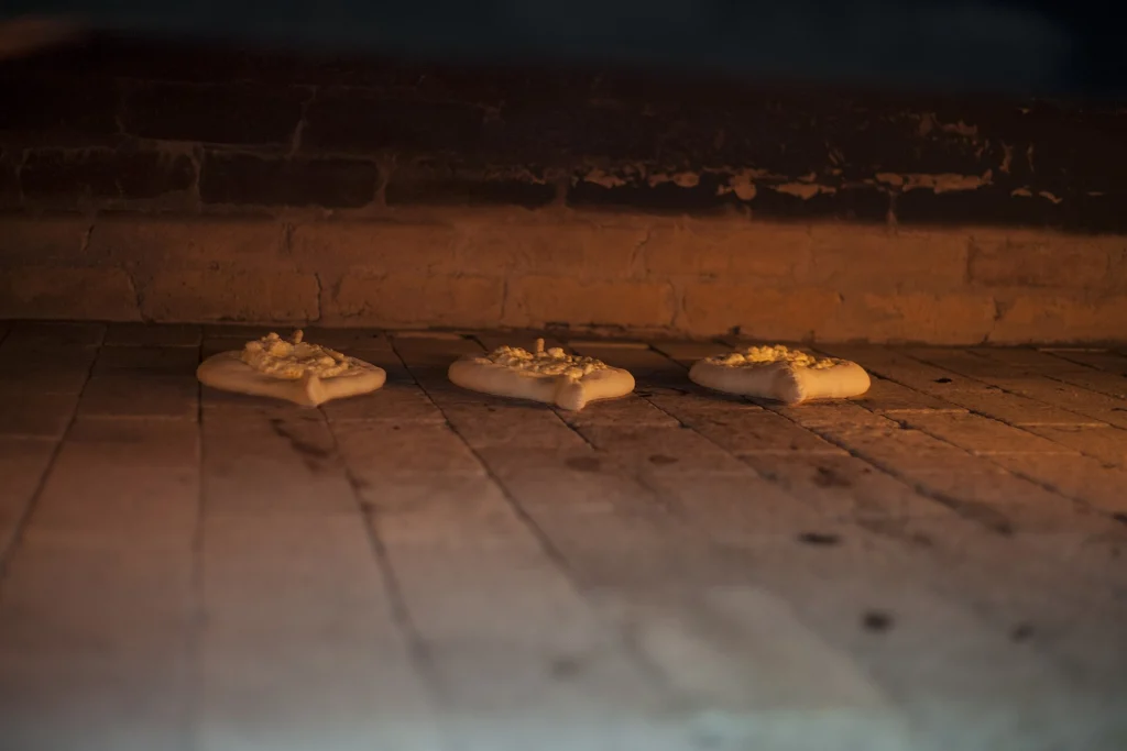 Three khachapuri breads baking inside a traditional stone oven with warm firelight.