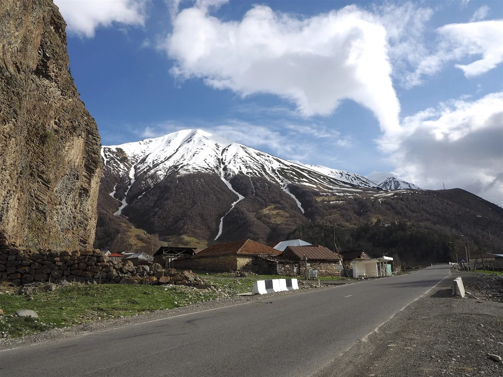 Snow-capped mountains and a quiet village line the road near Kazbegi, a classic Georgian landscape.