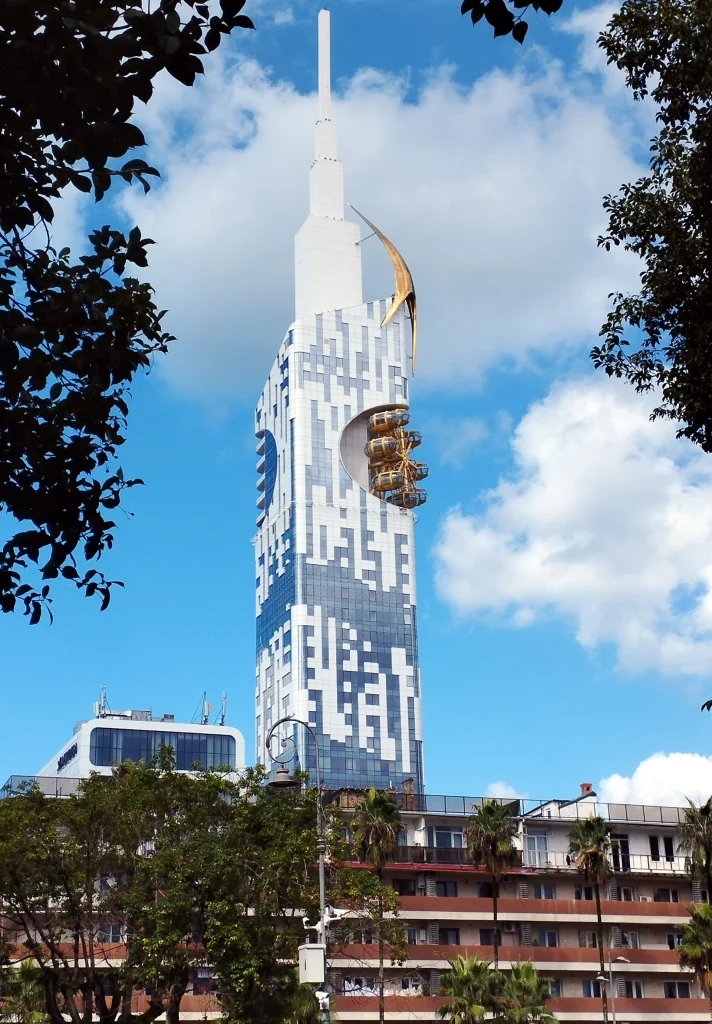 Batumi Tower skyscraper rising above Europe Square, framed by trees.
